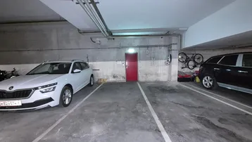 Geräumige Tiefgarage mit Betonwänden, zwei Stellplätzen, Fahrradaufhängung und Ladestation für Elektrofahrzeuge.