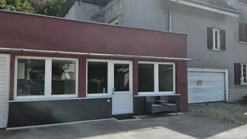 Au ßenansicht eines Gebäudes mit roter Fassade und Garagenzugängen, umgeben von Grün.