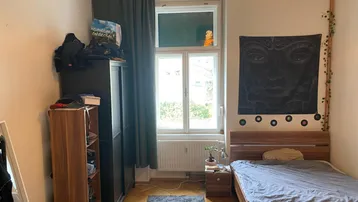 Gemütliches Schlafzimmer mit Parkettboden, großem Fenster und dunklen Vorhängen, hell beleuchtet.