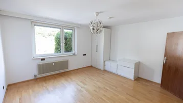 Helles Schlafzimmer mit Holzparkettboden, großem Fenster und weißem Kleiderschrank.