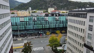 Blick von oben auf eine belebte Stadtstraße mit modernen Gebäuden und Bergen im Hintergrund.