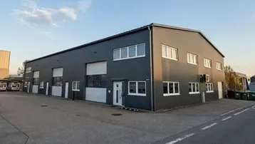 Modernes Gewerbegebäude mit dunkelgrauer Fassade, mehreren Rolltoren und großen Fenstern unter blauem Himmel.