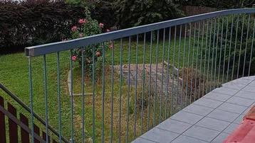 Geflieste Terrasse mit Metallgeländer und Blick auf einen grünen Gartenbereich.