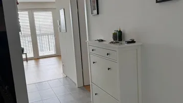 Heller Flur mit Fliesenboden, Schuhschrank und Zugang zu weiteren Räumen.