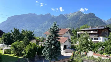 Panoramablick auf die umliegende Berglandschaft mit Wohnhäusern und viel Grün.