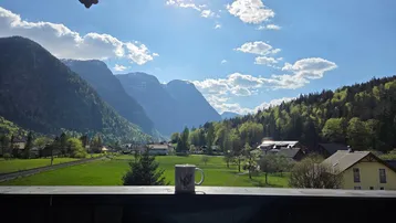 Sonnenverwöhnter Balkon mit atemberaubendem Blick auf die majestätische Berglandschaft und grüne Wiesen.