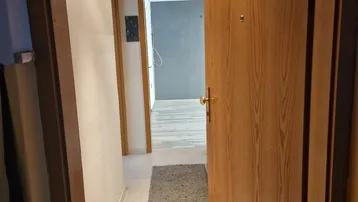 Flur mit Holztür und Deckenpaneelen, der zu weiteren Räumen führt.