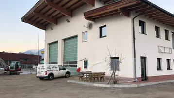 Modernes Gebäude mit großen Garagentoren, Holzdachüberstand und einem Lieferwagen davor.