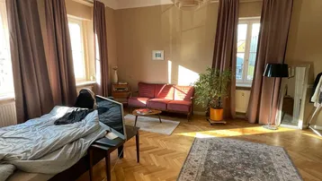 Helles Schlafzimmer mit Fischgrätparkett, gemütlichem Sofa und großem Teppich, gut gepflegt.
