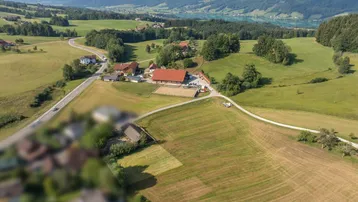 Ländliche Umgebung mit einem Anwesen, Reitplatz und einem See im Hintergrund, umgeben von grünen Hügeln.