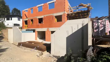 Neubau im Rohbau mit Ziegelwänden und Betonfundament unter blauem Himmel.