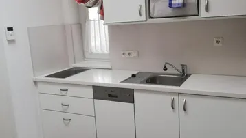 Funktionale Küche mit weißen Schränken, integriertem Geschirrspüler und Fenster über der Spüle.