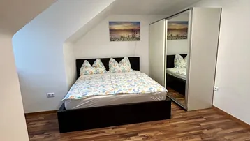Gemütliches Schlafzimmer mit Holzboden, Dachschrägen und einem großen Spiegelschrank.