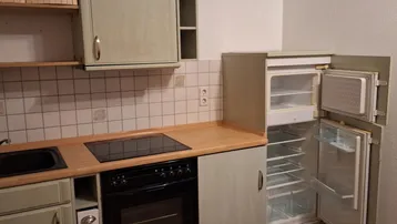 Helle Küche mit hellgrünen Schränken, Holztheke, integriertem Herd und Kühlschrank.