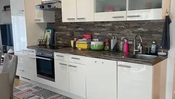Moderne Einbauküche mit weißen Hochglanzfronten, dunkler Arbeitsplatte und Holzakzenten.