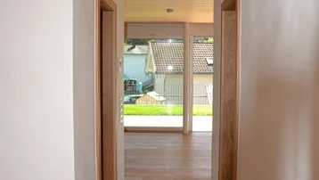 Heller Flur mit Holzboden und Holzdecke, der zu einem lichtdurchfluteten Außenbereich führt.