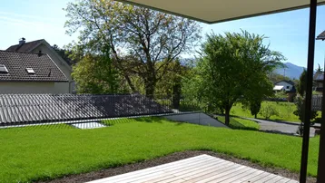 Große Holzterrasse mit angrenzendem Rasen und Blick auf die umliegende grüne Landschaft.