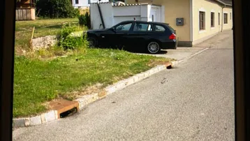 Gelbes Einfamilienhaus mit schwarzem Auto davor und Grünfläche im Vordergrund.