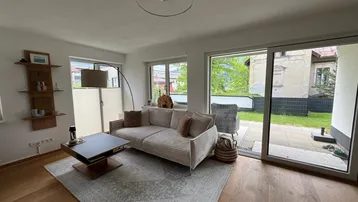 Helles Wohnzimmer mit beigem Sofa, Holzboden und Zugang zur Terrasse mit Blick ins Grüne.
