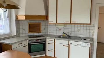 Funktionale Küche mit weißen Schränken, Holzdetails, Fliesenboden und integrierten Geräten.