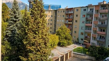 Weitblick über Wohngebäude und Grünflächen mit Bergen im Hintergrund unter blauem Himmel.