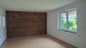 Heller Wohnraum mit einer markanten Holzwand und Blick ins Grüne durch das Fenster.