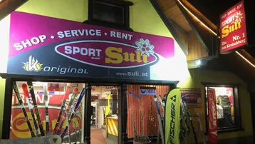 Beleuchtete Fassade eines Sportgeschäfts bei Nacht mit Skiern und Snowboards in den großen Schaufenstern.