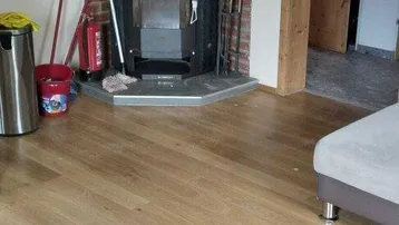 Gemütliches Wohnzimmer mit Holzofen, Holzboden und Zugang zu weiteren Räumen.