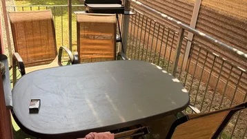 Gemütlicher Balkon mit Esstisch, Stühlen und Grill, umgeben von viel Grün.
