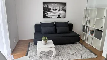 Gemütliches Wohnzimmer mit Schlafsofa, modernem Teppich und dekorativem Wandbild.