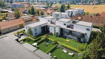 Moderne Wohnanlage mit Gemeinschaftsgarten und Spielplatz, umgeben von ländlicher und städtischer Bebauung.