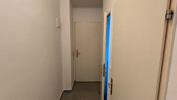 Langer, schmaler Flur mit hellen Wänden und grauem Fliesenboden, der zu weiteren Räumen führt.