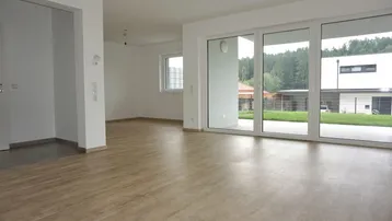 Helles, leeres Wohnzimmer mit großen Fenstern und Zugang zur Terrasse, bereit für die Einrichtung.