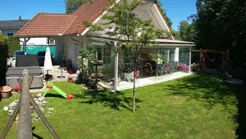 Großzügiger Gartenbereich mit Rasenfläche, Spielgeräten und einem Wintergarten am Haus.