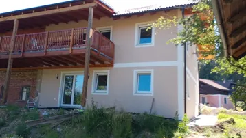 Modernes Wohnhaus mit Balkon und heller Fassade, umgeben von viel Grün und Bäumen.