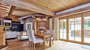 Gemütlicher Wohn-Essbereich im alpinen Stil mit Holzbalken, Esstisch und Zugang zur Terrasse.