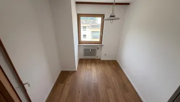 Kleines Zimmer mit Laminatboden, Fenster und Heizkörper, ideal als Kinder- oder Arbeitszimmer.