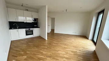 Heller offener Wohnbereich mit integrierter Küchenzeile, Parkettboden und Zugang zu einem Fenster.