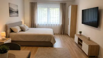 Helles Schlafzimmer mit Doppelbett, modernem Kleiderschrank, Wand-TV und Laminatboden, ideal für ein Studio-Apartment.