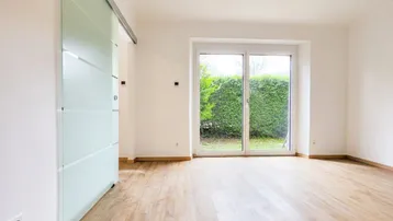 Geräumiger Wohnbereich mit Laminatboden und einer modernen Glasschiebetür zum Garten.