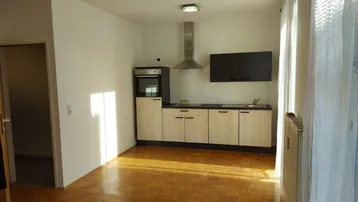 Helle Küchenzeile mit Holzparkettboden, modernen Schränken und integrierten Geräten.