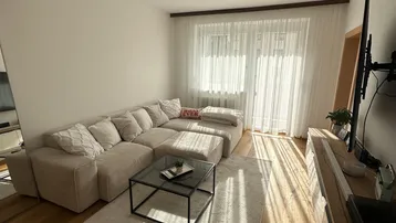 Helles Wohnzimmer mit beigem Ecksofa, Holzboden und moderner Deckenbeleuchtung.