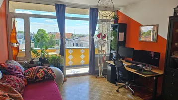 Helles Wohnzimmer mit Parkettboden, Schreibtisch und Zugang zu einem sonnigen Balkon.