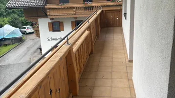 Langer Balkon mit Holzbalkonbrüstung und Blick auf ein traditionelles Gebäude und grüne Umgebung.