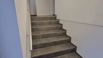 Helles Treppenhaus mit gefliesten Stufen, modernem Handlauf und indirekter Beleuchtung.