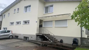 Vorderansicht eines gepflegten Wohngebäudes mit Eingangsbereich, Fenstern und Parkplatz.