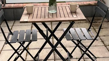 Gemütliche Terrasse mit Holztisch, zwei Stühlen und Blumen, ideal für entspannte Stunden im Freien.