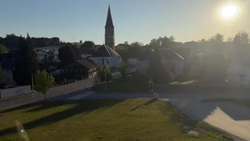 Panoramablick auf ein Dorf mit Kirchturm, umgeben von grünen Feldern bei Sonnenuntergang.