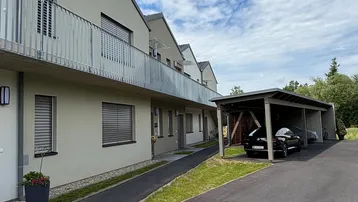 Moderne Reihenhäuser mit Balkonen und einem Carport unter blauem Himmel.
