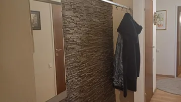 Heller Eingangsbereich mit dekorativer Steinwand, großem Spiegel und Garderobe auf Holzfußboden.